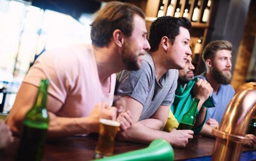 Group of friends watching a live game at a sports bar with beers